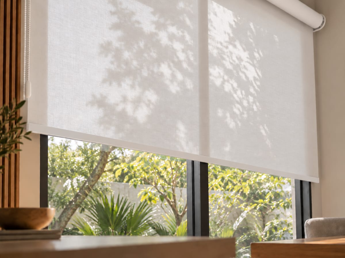 Store enrouleur en tissu blanc filtrant le soleil devant une fenêtre