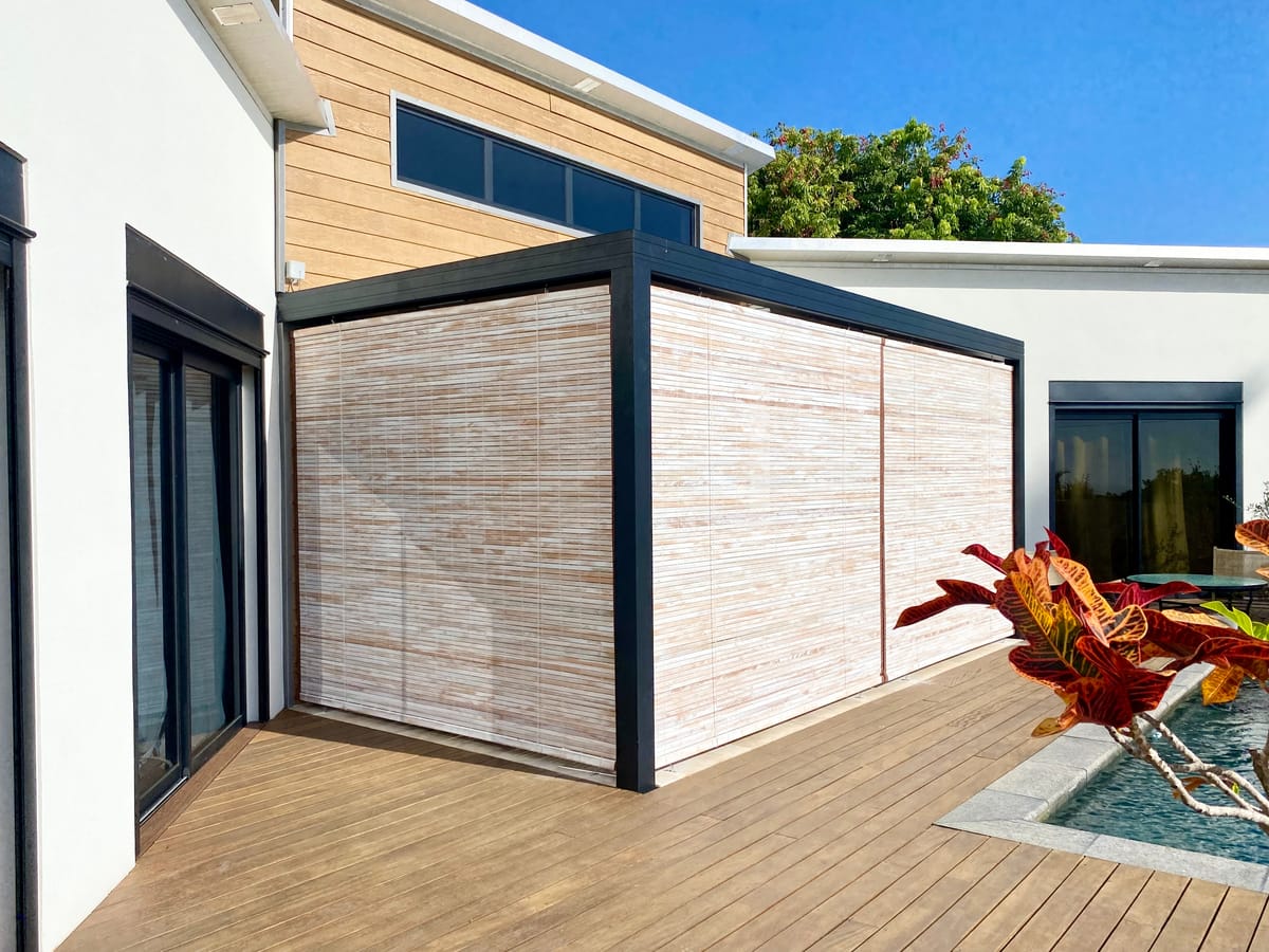 Stores mauriciens à lames claires fermant une pergola sur une terrasse en bois